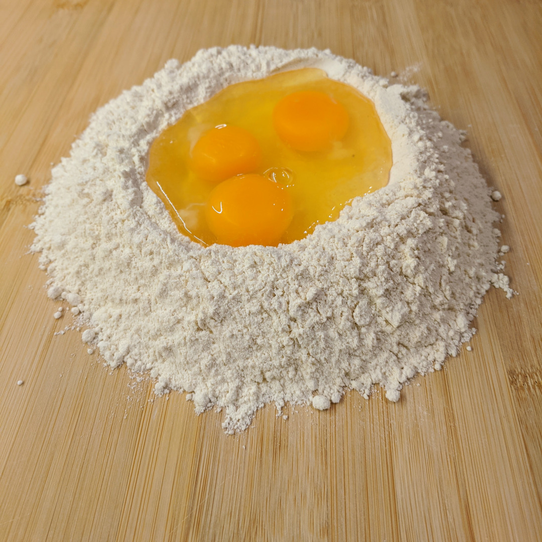 A pile of flour with the contents of three eggs in a small well in the center