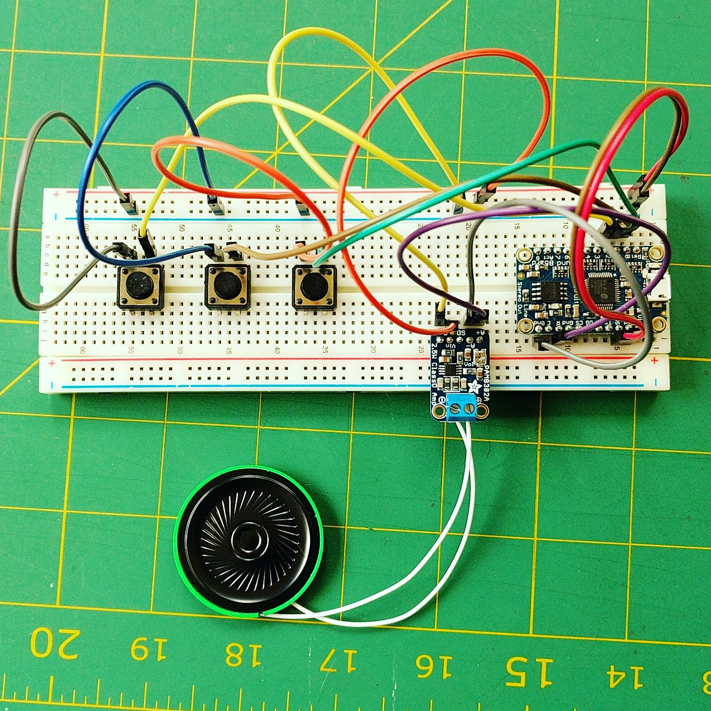 Breadboard with three buttons, two circuit boards, and a speaker.