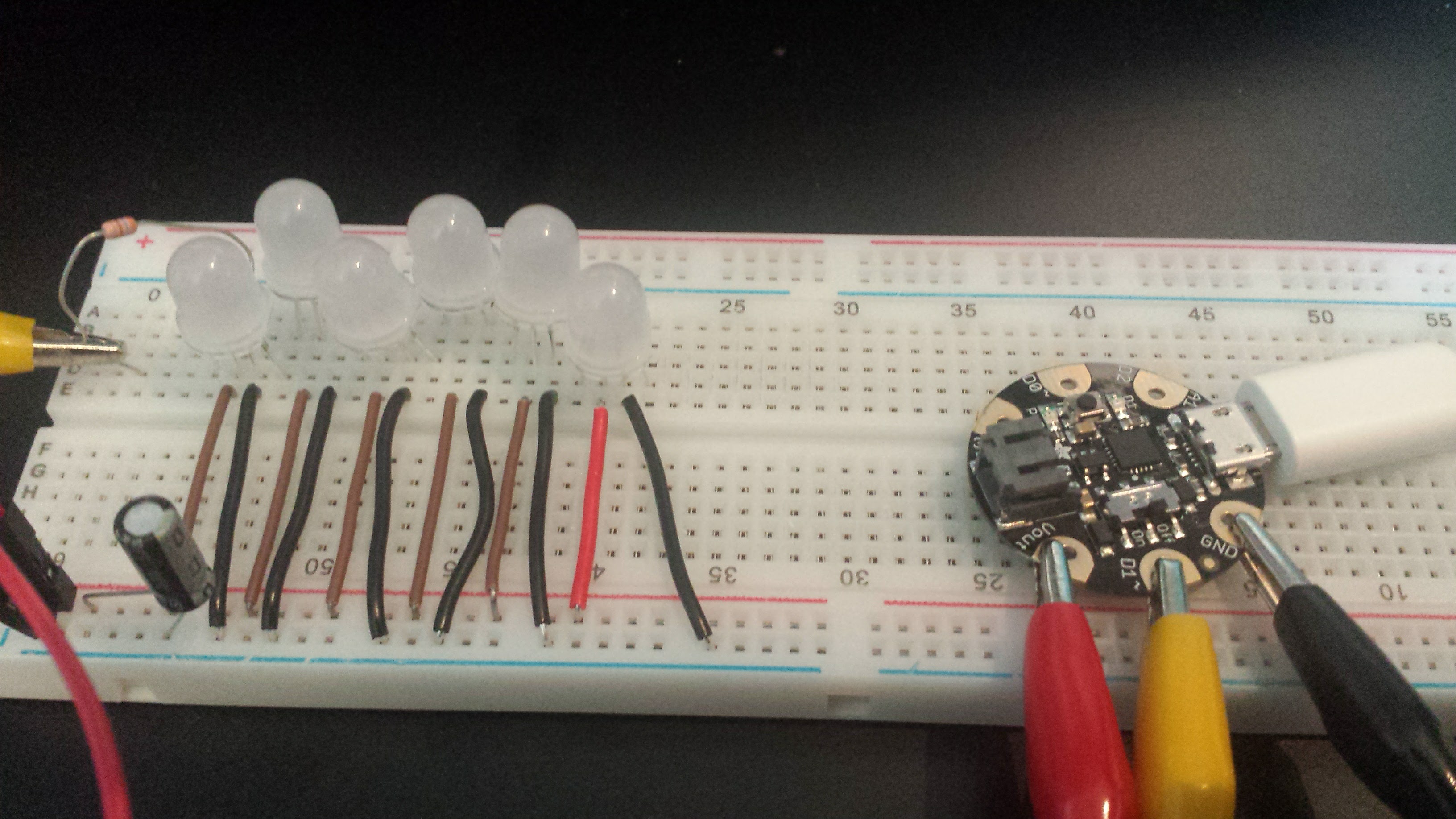A microcontroller connected with alegator clips to a breadboard containing a capacitor and six LEDs