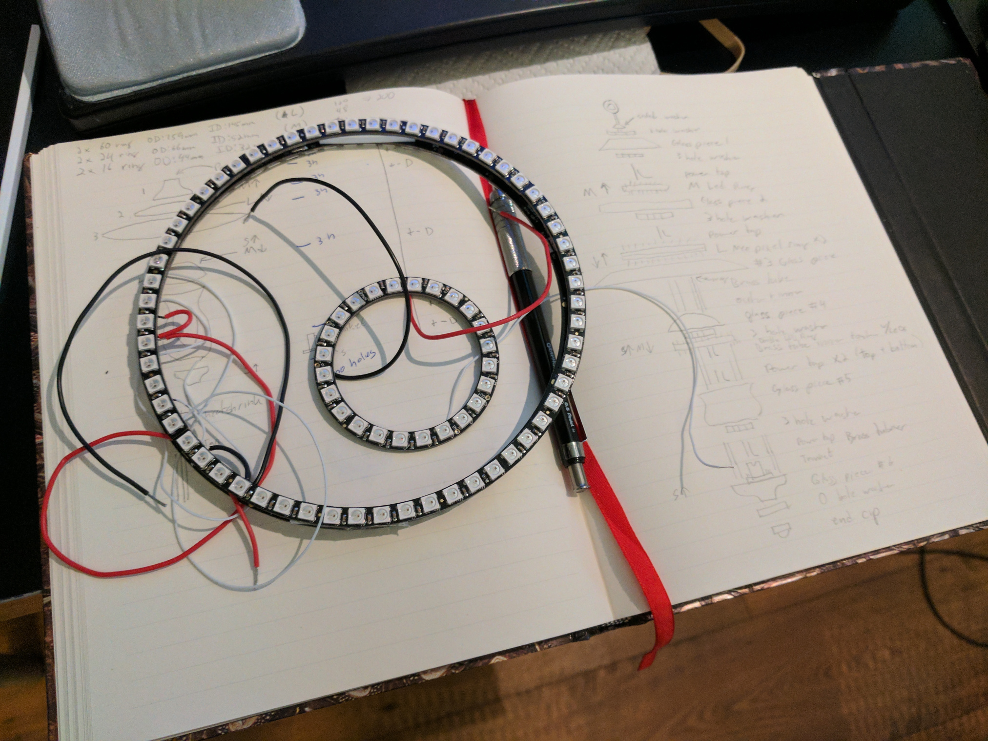 An open notebook with a diagrom of the lantrn.  A pencil and a pair of LED rings, one large, one small, sit on top.