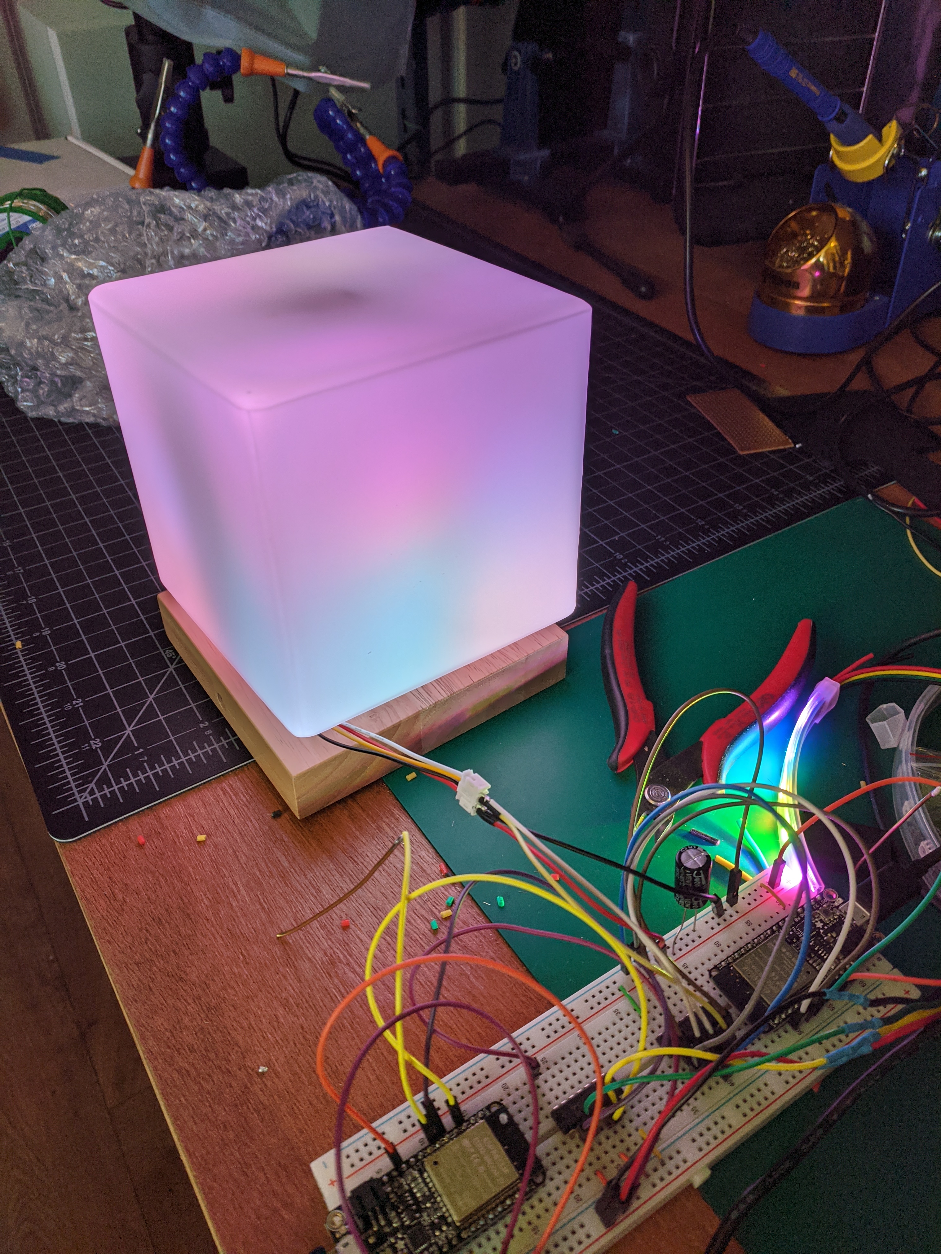 ESP32 microcontroller on a breadboard with wires leading into a cube lamp glowing in several colors