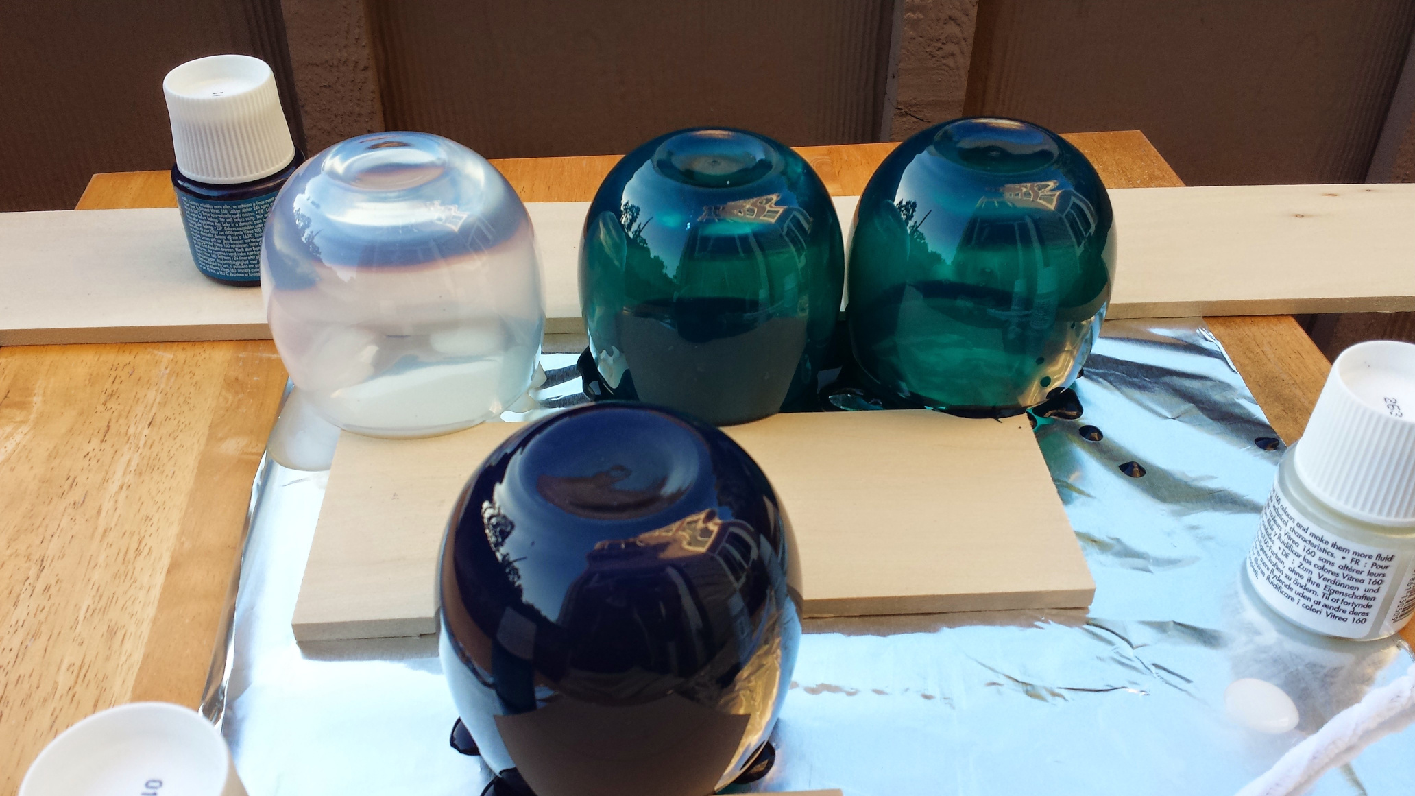 A series of four glass vases with different color treatments sitting upside down on a work bench.