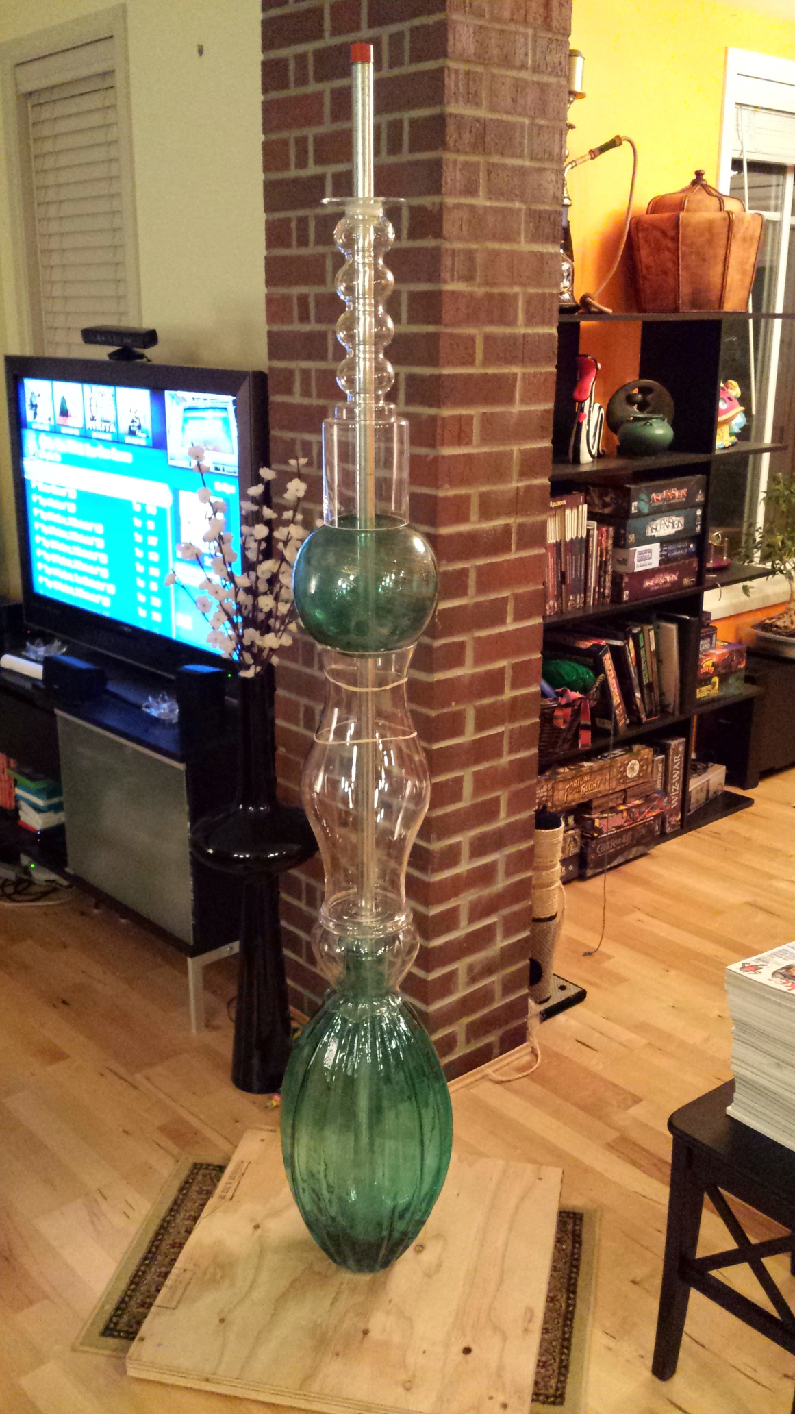 A square plywood base with a 6 foot tall metal rod pointing upward. A stack of glass vases rises around the pole.