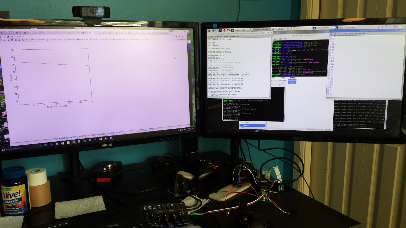 A pair of monitors showing graphs and terminal windows, with electronics sitting below the monitors.