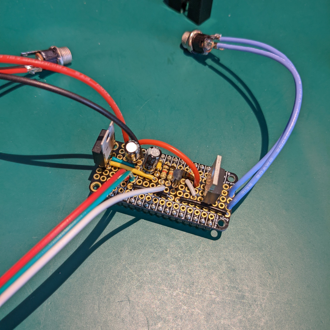A proto board in the feather form factor with mounted electronics and wires leading to barrel sockets