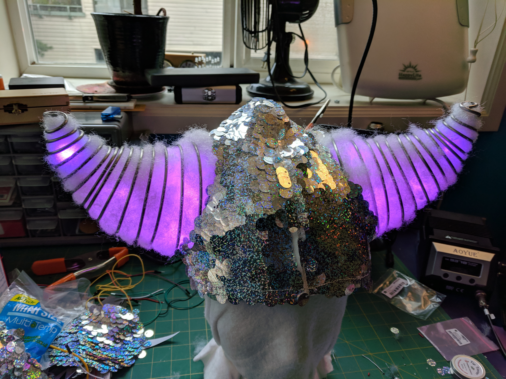 Assembled helmet with holographic sequin fabric covering and stuffed horns glowing with LEDs