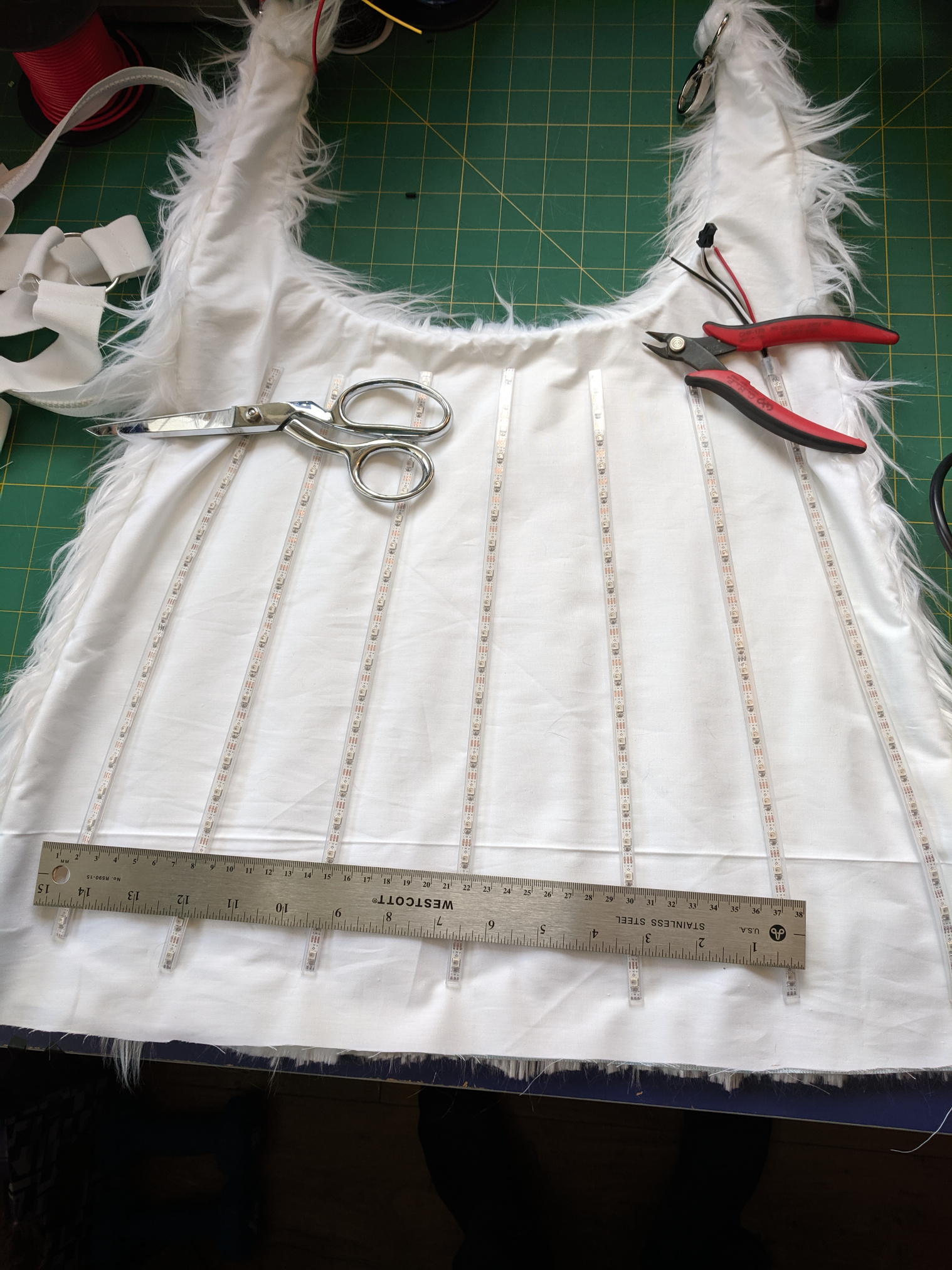 A white fur capelet lying upside down on a work surface with LED strips laid out vertically