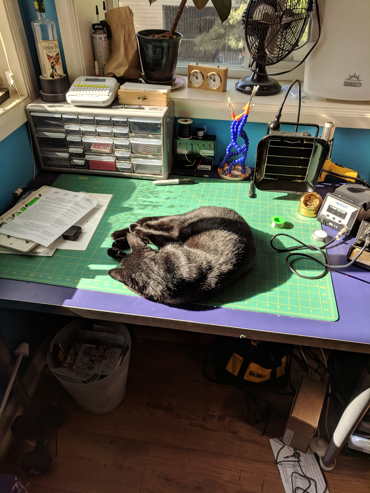 A black cat laying on a desk set up as a simple electonrics work bench.